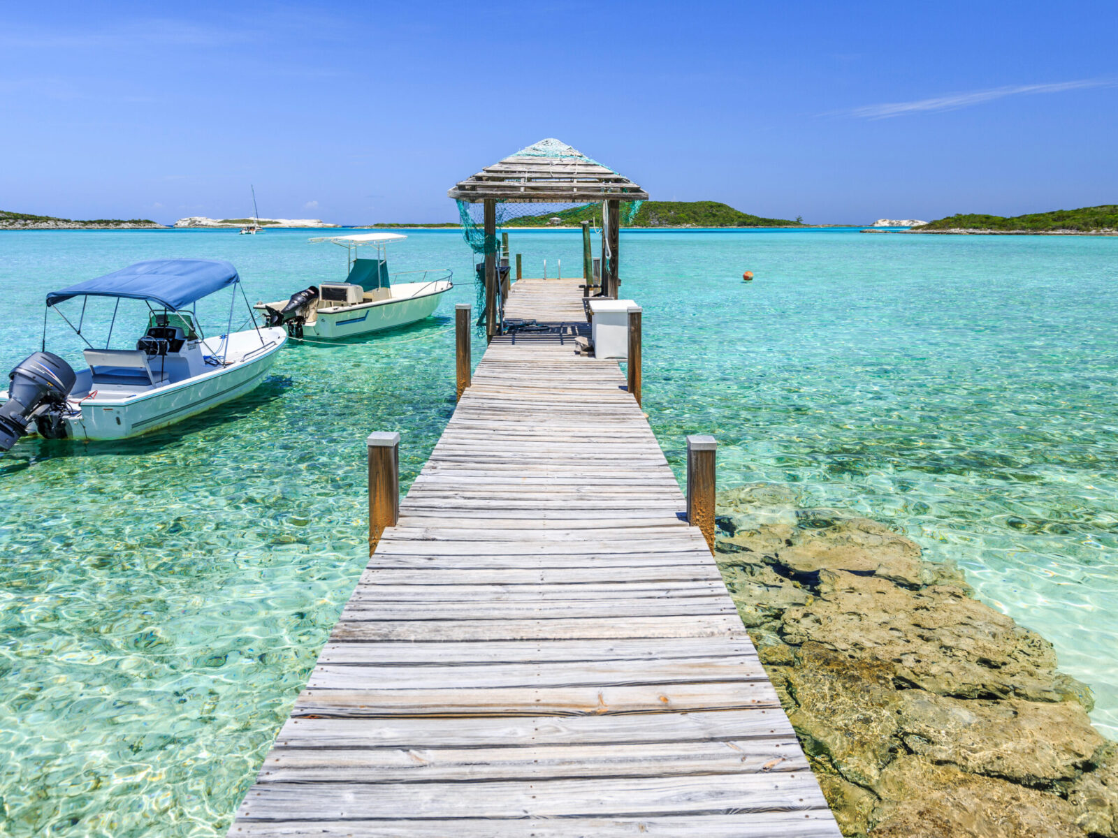 A,Wood,Pier,Leads,To,Moored,Boats,And,Clear,Tropical